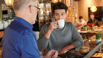 Mann unterhält sich mit einem Kollegen und trinkt Kaffee