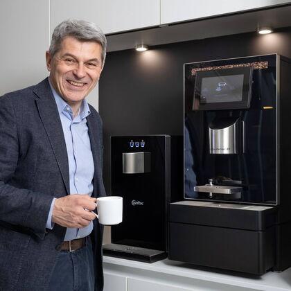 Volker Breid genießt seinen Kaffee vor dem Kaffeevollautomaten und Wasserspender von Kaffee Partner