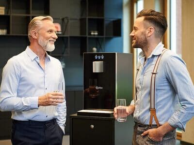 Zwei Männer trinken Wasser vor einem Wasserspender Zwei Männer unterhalten sich und trinken Wasser vor einem Wasserspender im Büro
